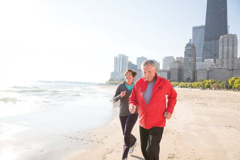 A man and woman running on beach with chicago in the background
