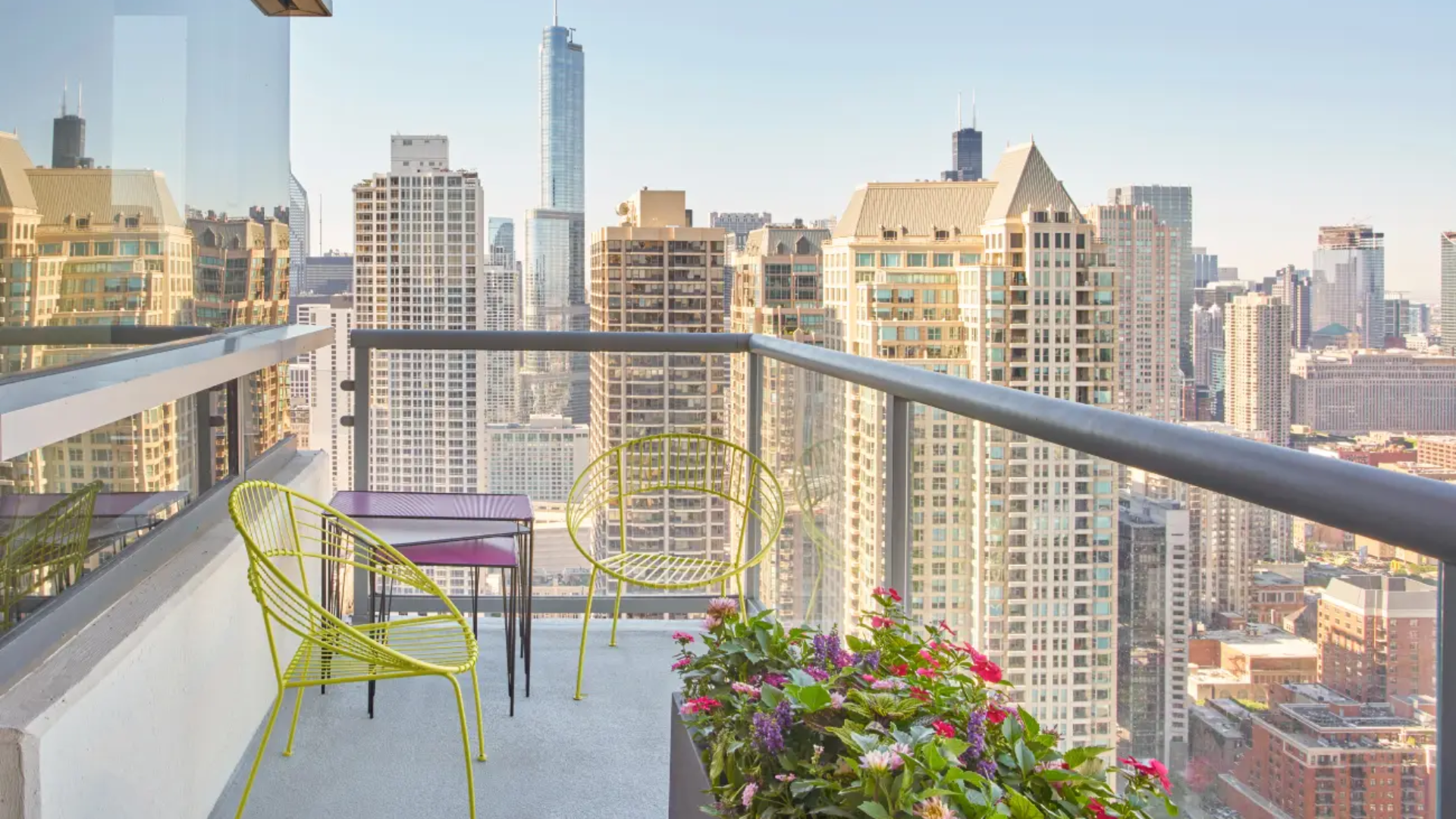 Private balcony view from The Clare in Chicago with patio seating, flower planter, and sweeping views of the downtown skyline and iconic skyscrapers.