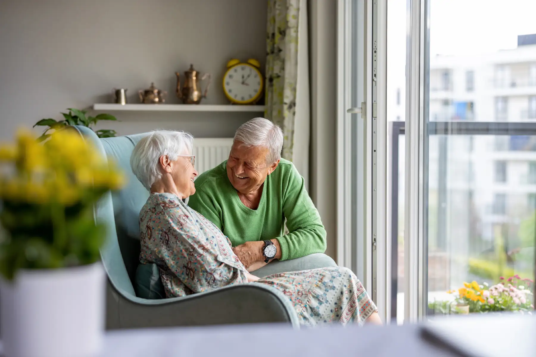 a senior couple sitting at home laughing together as they look out the window